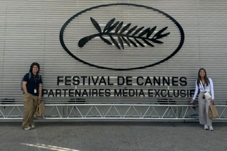 two students stand in front of a Cannes Film Festival sign 